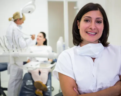 A confident doctor stands outside the hospital while another doctor is treating a patient's skin.